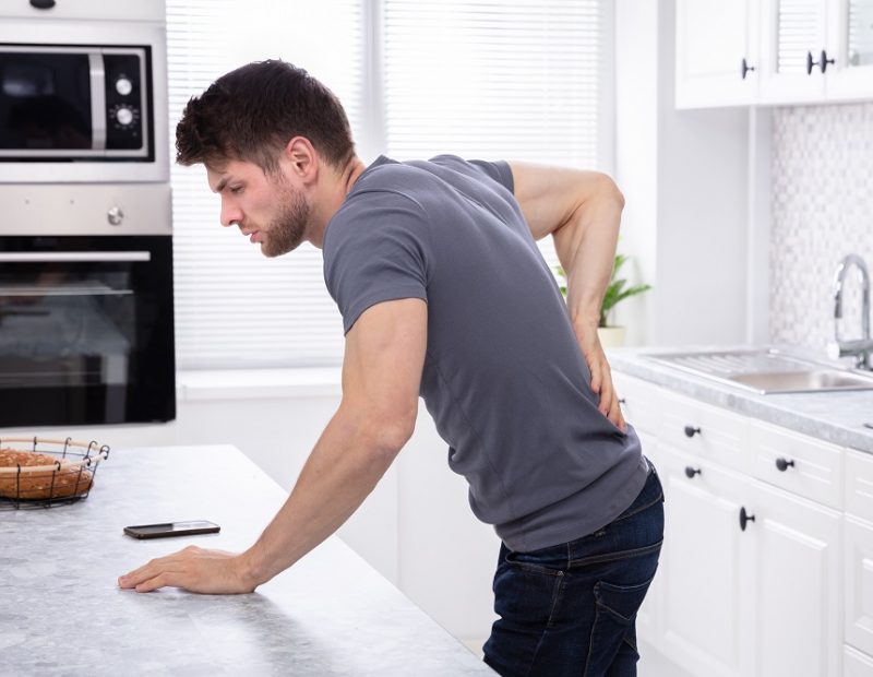 Side View Of Man Standing In Kitchen Suffering From Back Pain